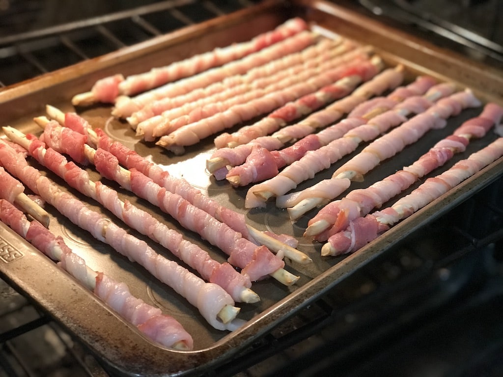 Bacon wrapped breadsticks on a baking sheet.