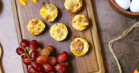 Egg bites on a wooden cutting board with oranges and grapes for Pinterest.