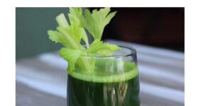 Glass of green juice with celery garnish.