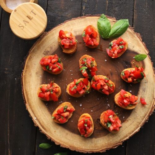 tomato mixture on bread slices on wood plank with salt container on black table