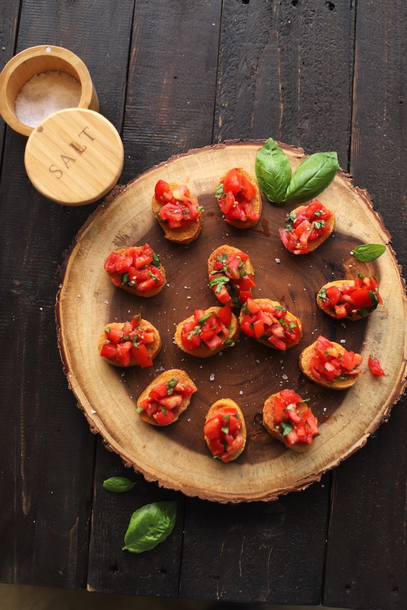 tomato mixture on bread slices on wood plank with salt container on black table