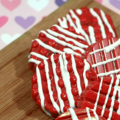 Red chocolate covered Oreo cookies with white chocolate drizzle on a wood cutting board.