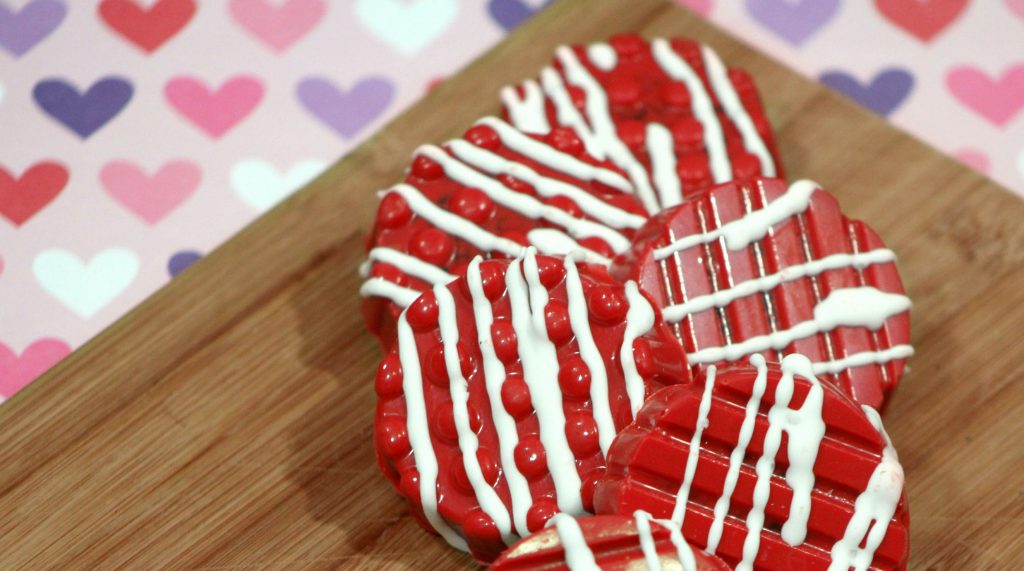 Red chocolate covered Oreo cookies with white chocolate drizzle on a wood cutting board.