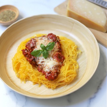 Chicken parmesan served over spaghetti squash on a tan plate.