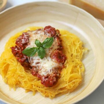 Chicken parmesan served over spaghetti squash on a tan plate.