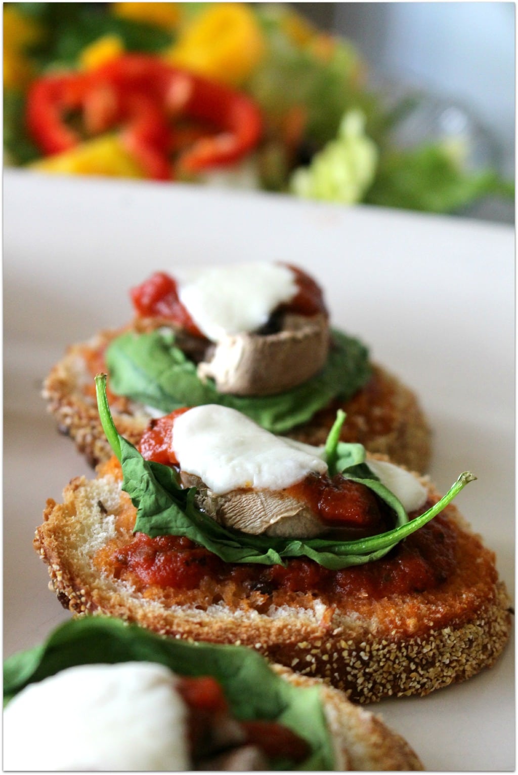 Bread topped with mozzarella, spinach, mushroom, sauce, and more mozzarella.