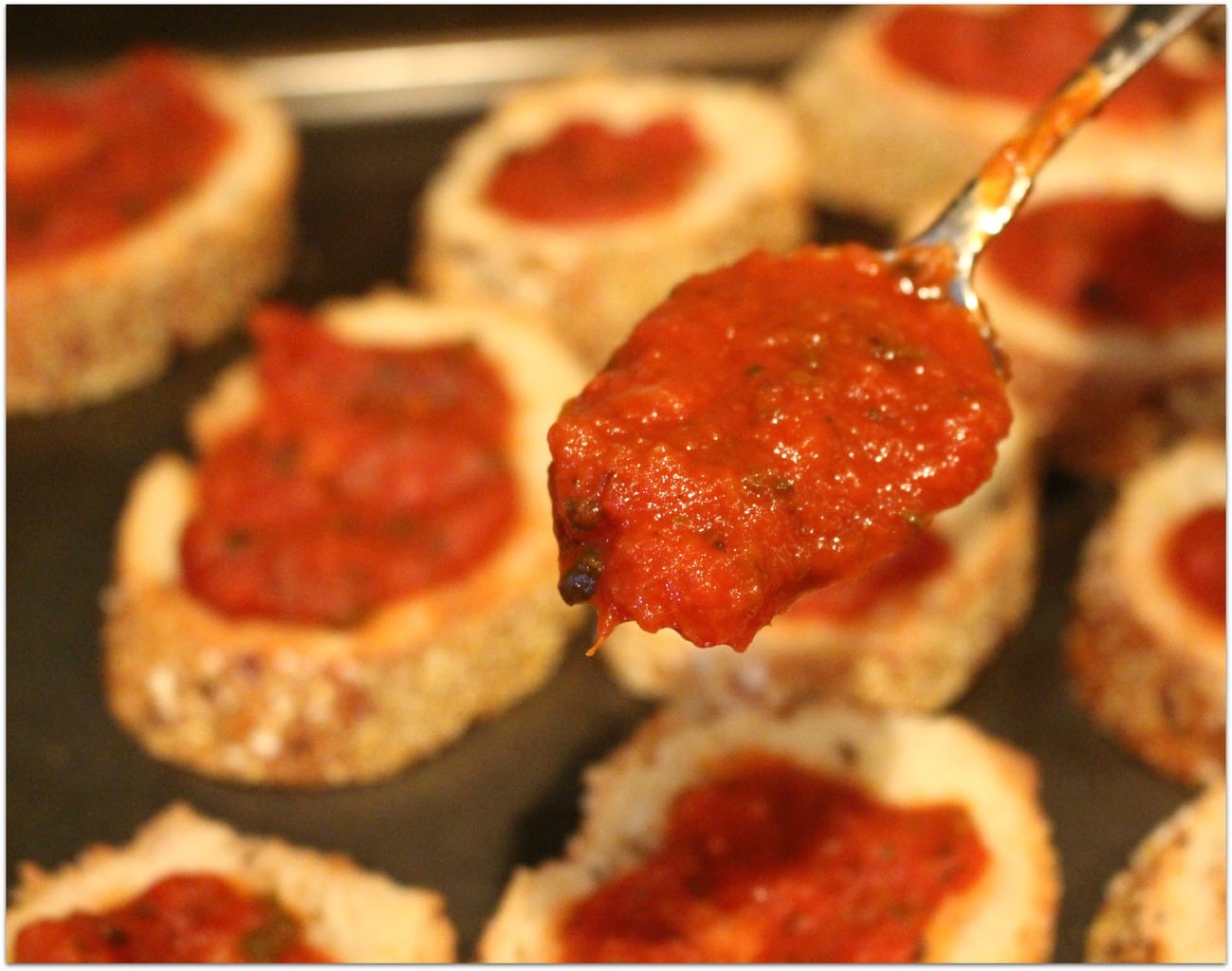 Spoon of marinara sauce with bread and sauce in background.