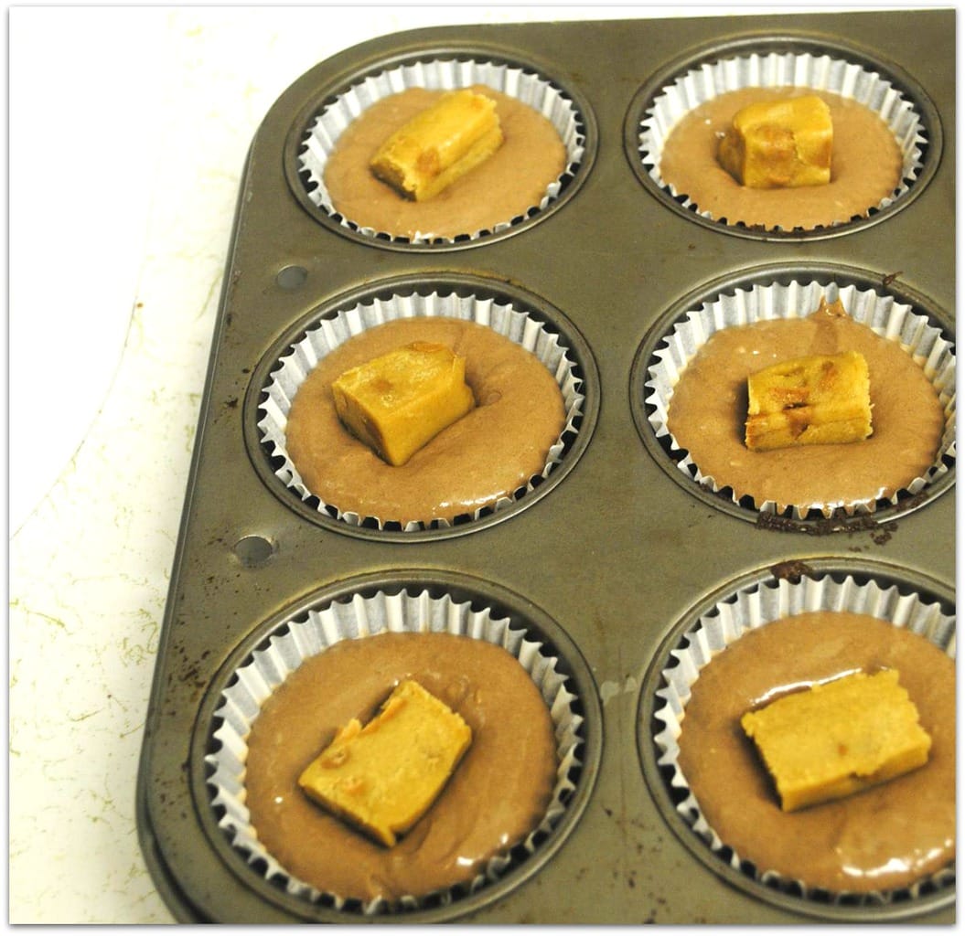 Cupcake batter in pan with pieces of cookie dough in center.