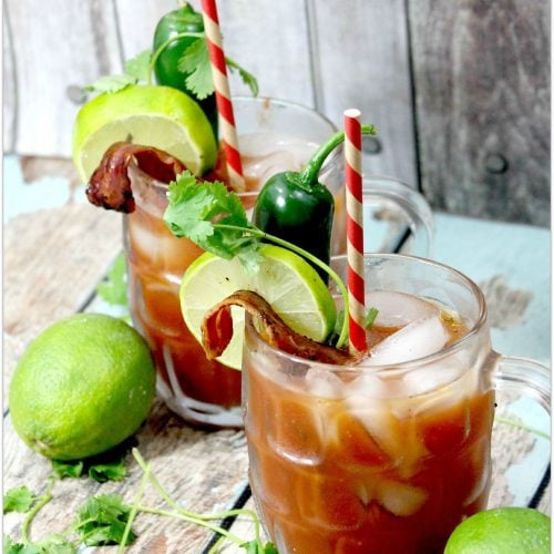 Two Bloody Mary cocktails with lime, jalapeno, cilantro, and straw.