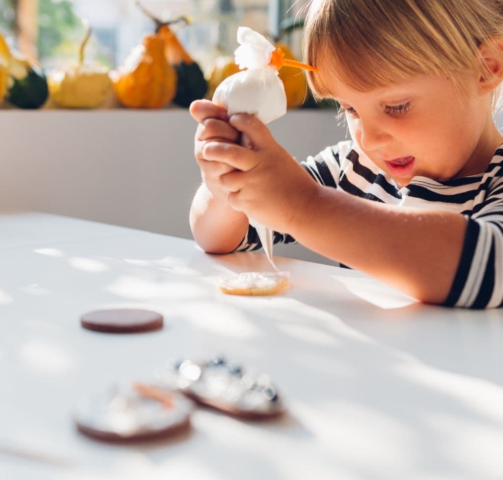 young girl decorating cookies on a white table