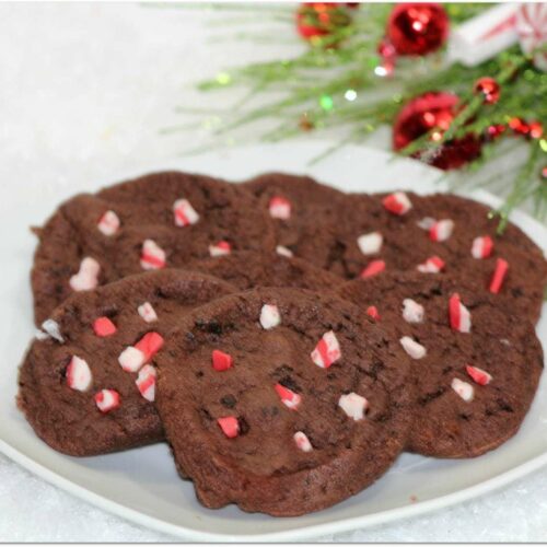 Chocolate cookies with peppermint bits on a white plate in front of Christmas decor.