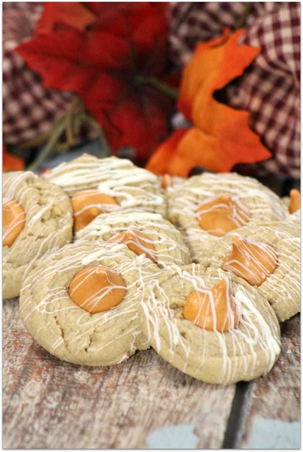 Thumbprint cookies with white icing drizzle on a wood board with fall leaves.