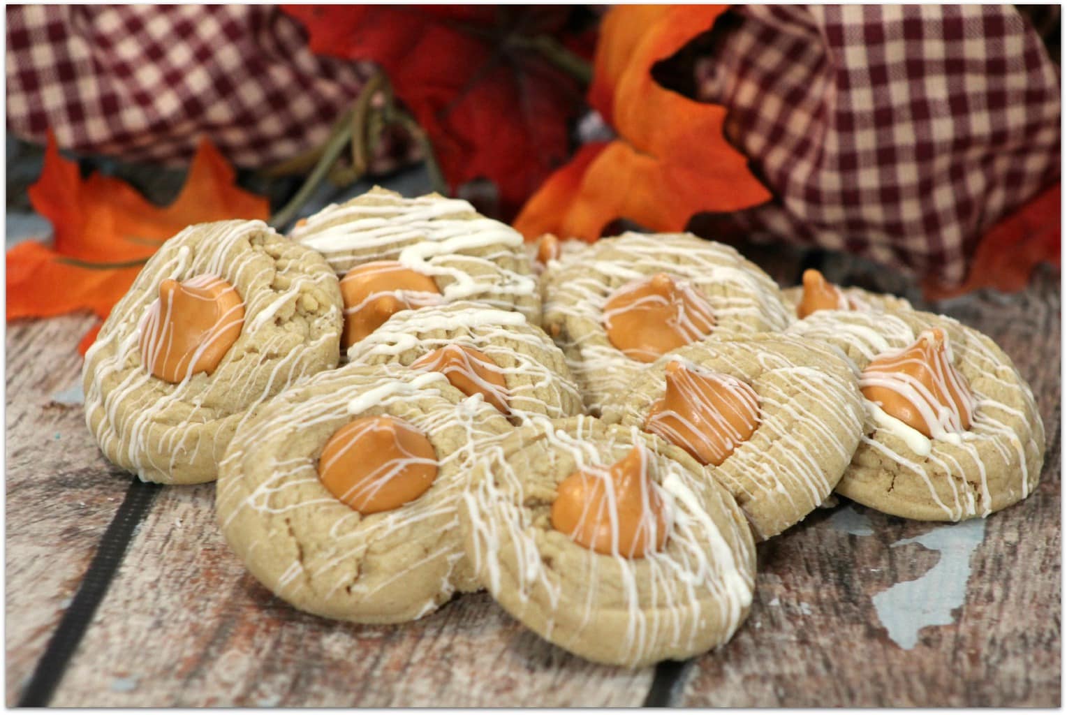 Thumbprint cookies with white icing drizzle on a wood board with fall leaves.