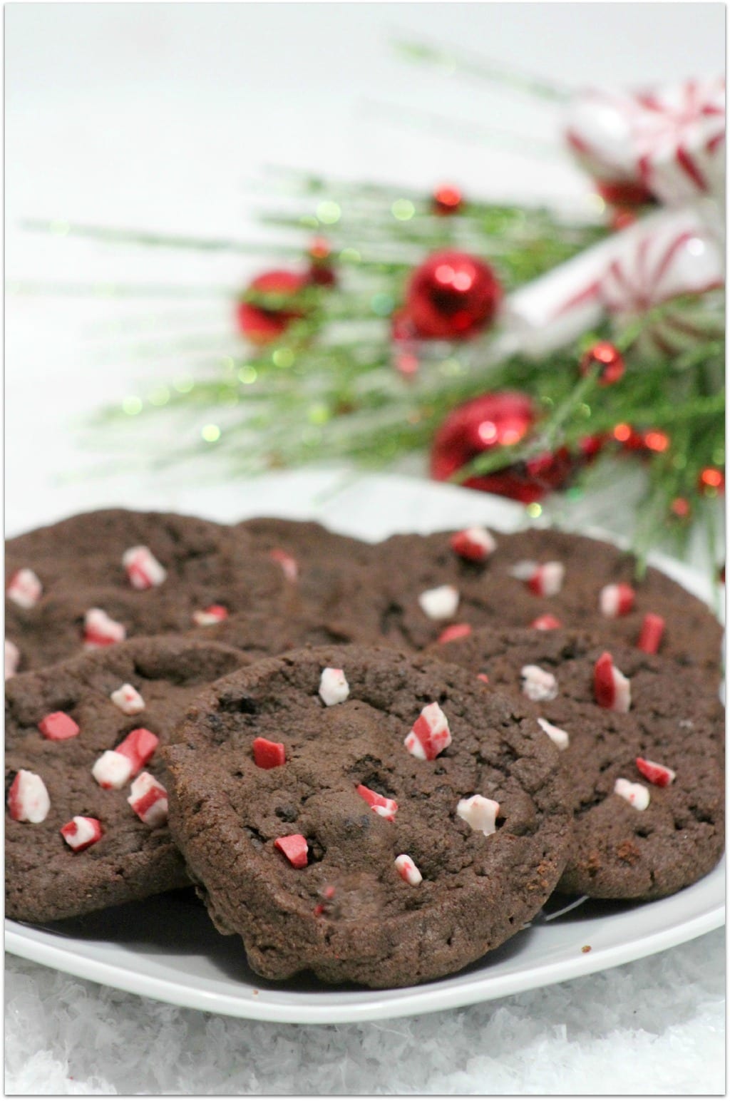 Chocolate cookies with candy cane pieces on a white plate with Christmas decor.