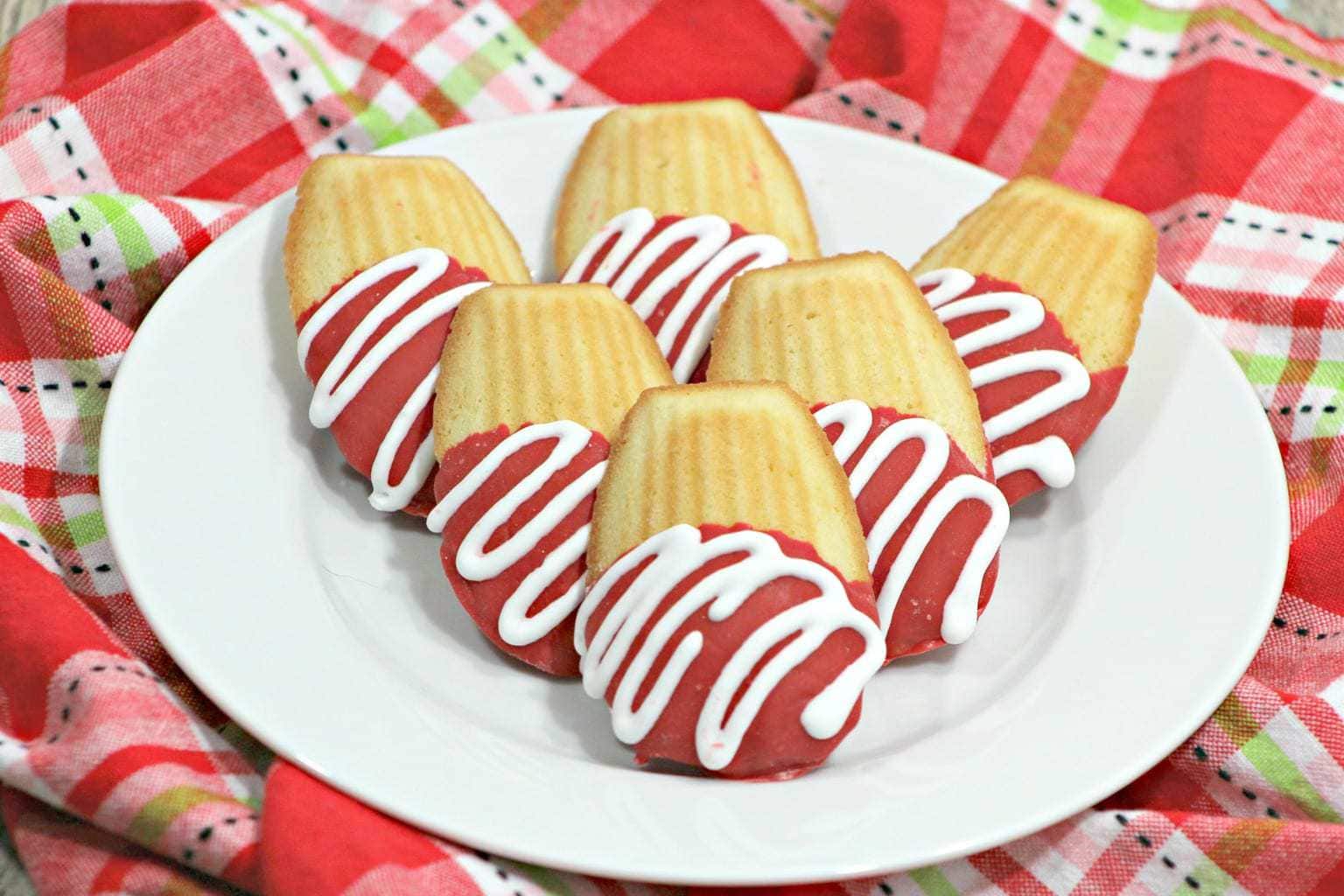Red and white Chocolate Covered Madeleine cookies on a white plate on a red plaid cloth.