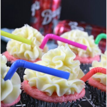 Pink cupcakes with yellow frosting and colored straws on a wire rack.