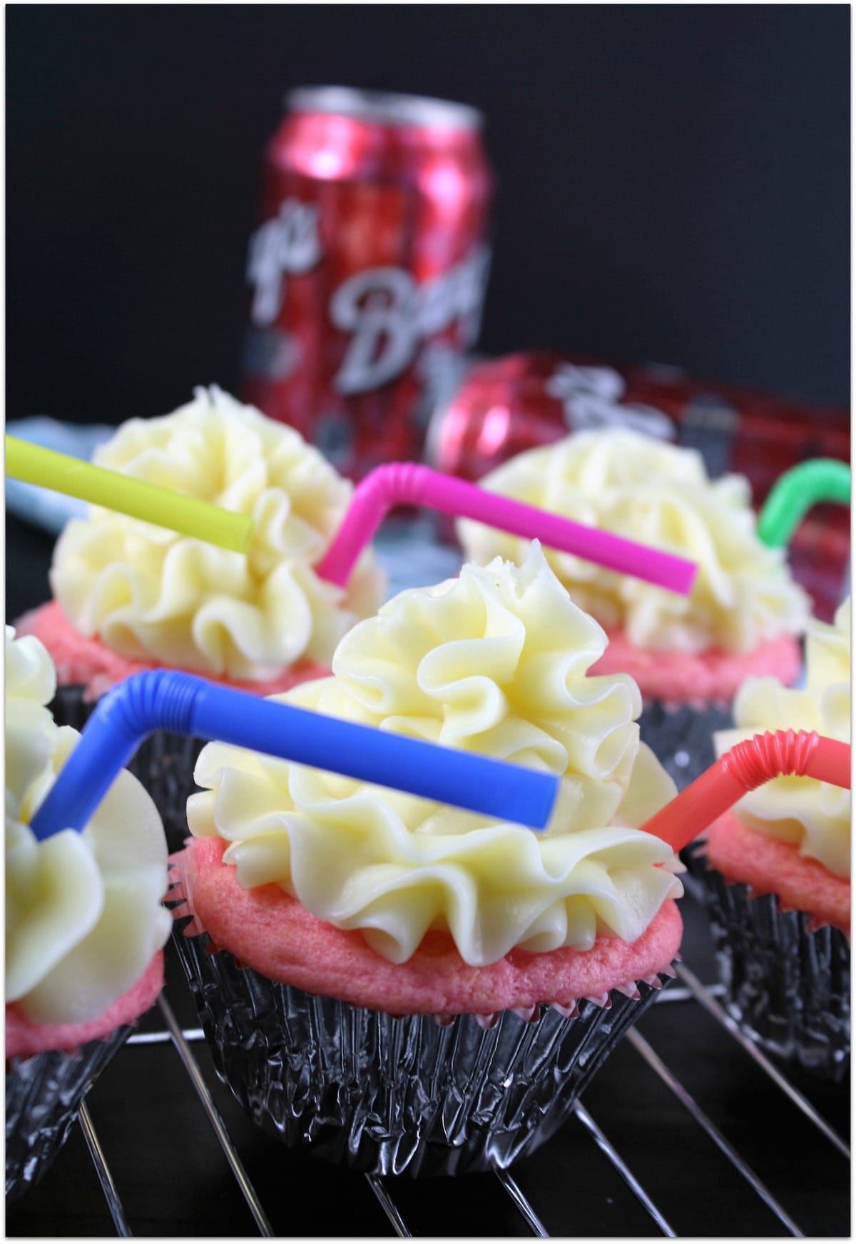 Pink cupcakes with yellow frosting with multi-colored straws in each one, set on a wire rack.