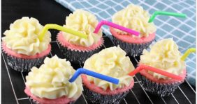 Pink cupcakes with yellow icing and a straw on a wire rack.