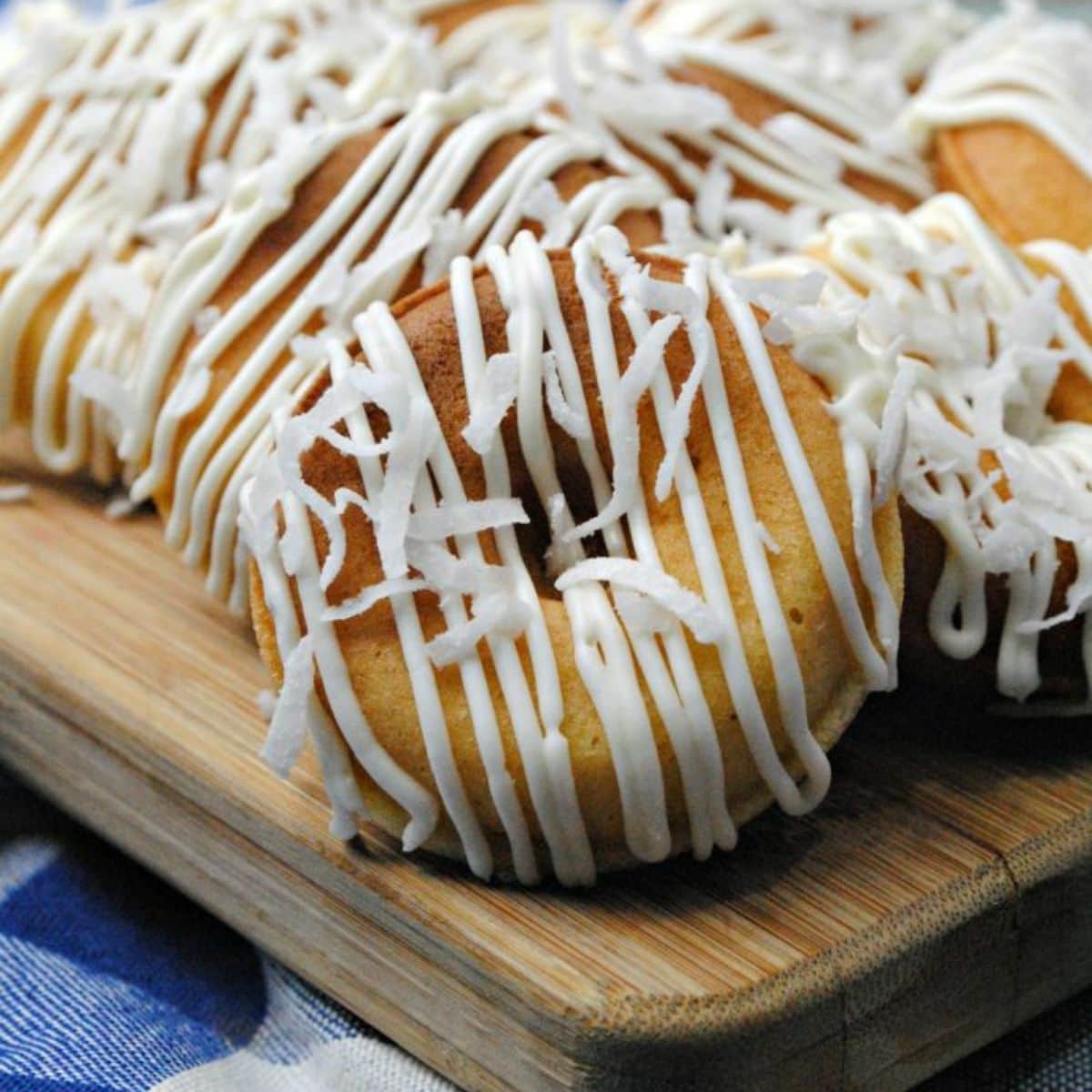 Doughnuts with icing drizzle on a wood cutting board.