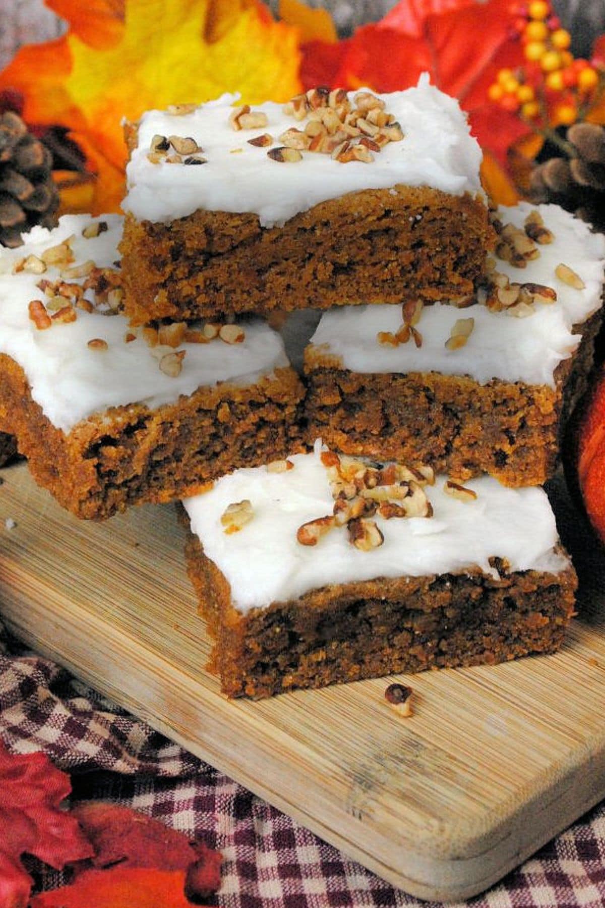 Pumpkin bars with cream cheese icing on wood board with pumpkin and fall leaves.