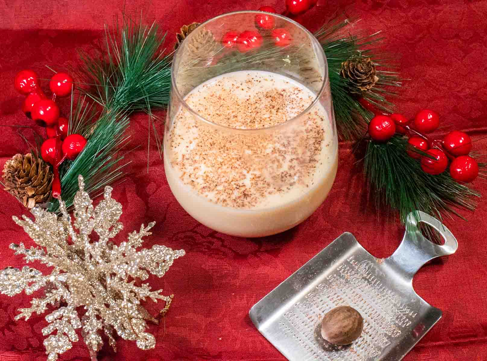 Glass of egg nog on a red tablecloth with festive holiday decor.