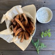 crispy oven sweet potato fries in a paper lined basket, with dip and herbs on a black board