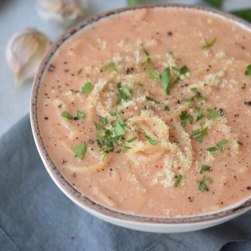 Creamy tomato pasta soup with fresh basil in a white bowl.