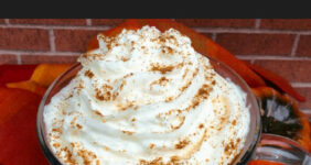 Frappuccino topped with whipped cream and pumpkin spice on an orange cloth with bricks in background.