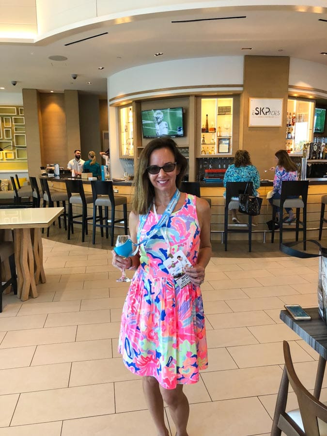 Woman in front of a bar in multi colored dress holding a wine glass.