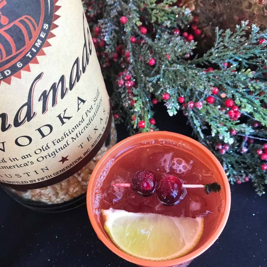 Bottle of Tito's Vodka and and cocktail with cranberries and lemon.