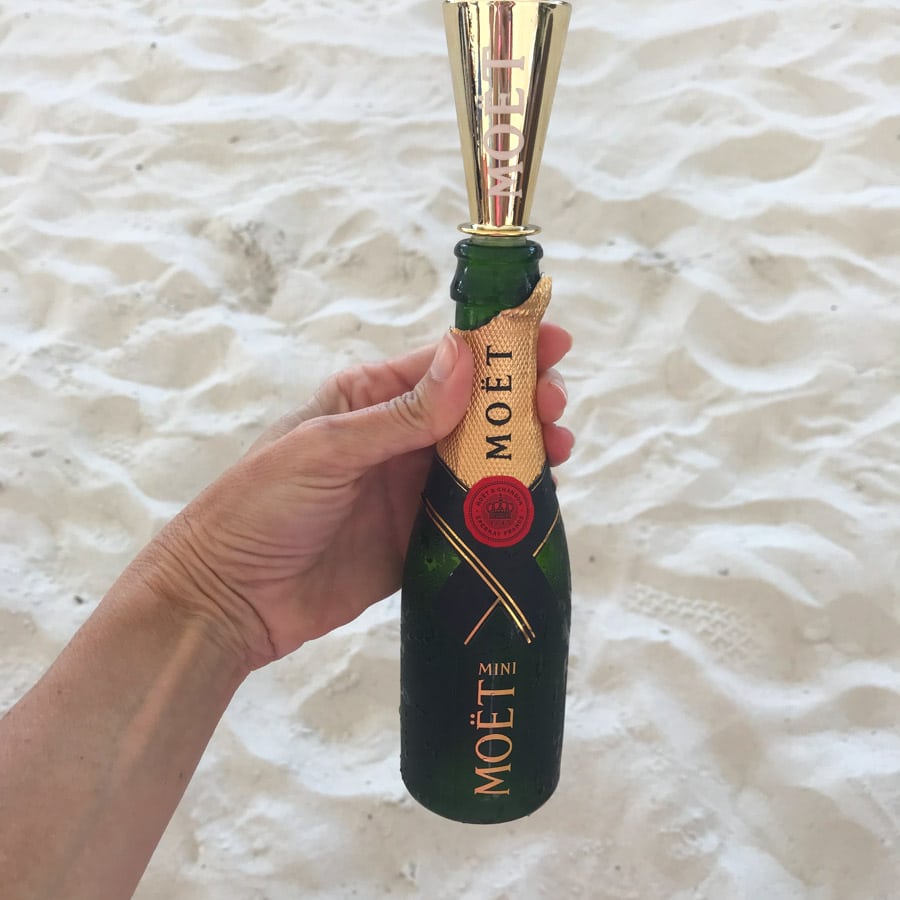 Hand holding a small bottle of Moet champagne with sand in the background