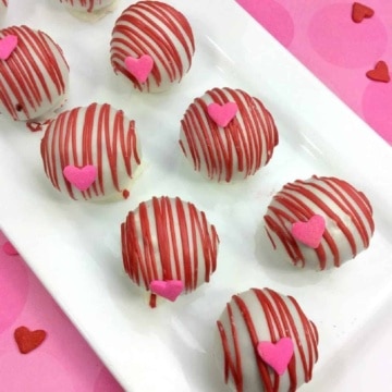 White chocolate covered cake balls with pink chocolate drizzle and candy heart sprinkles.