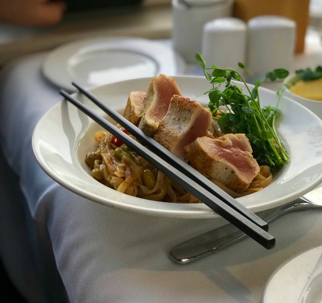 Seared tuna over noodles with chopsticks in a white bowl.