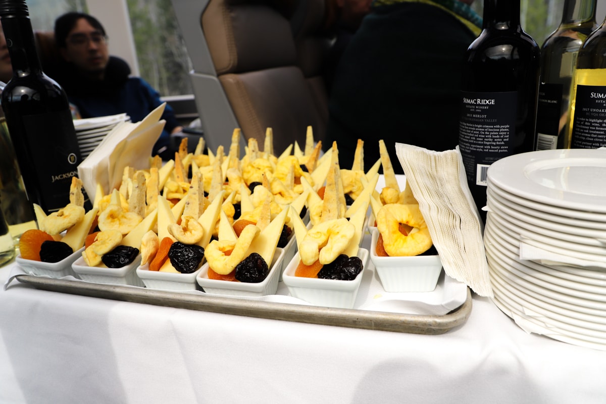 Snacks of dried fruit on a white tablecloth with bottles of wine.