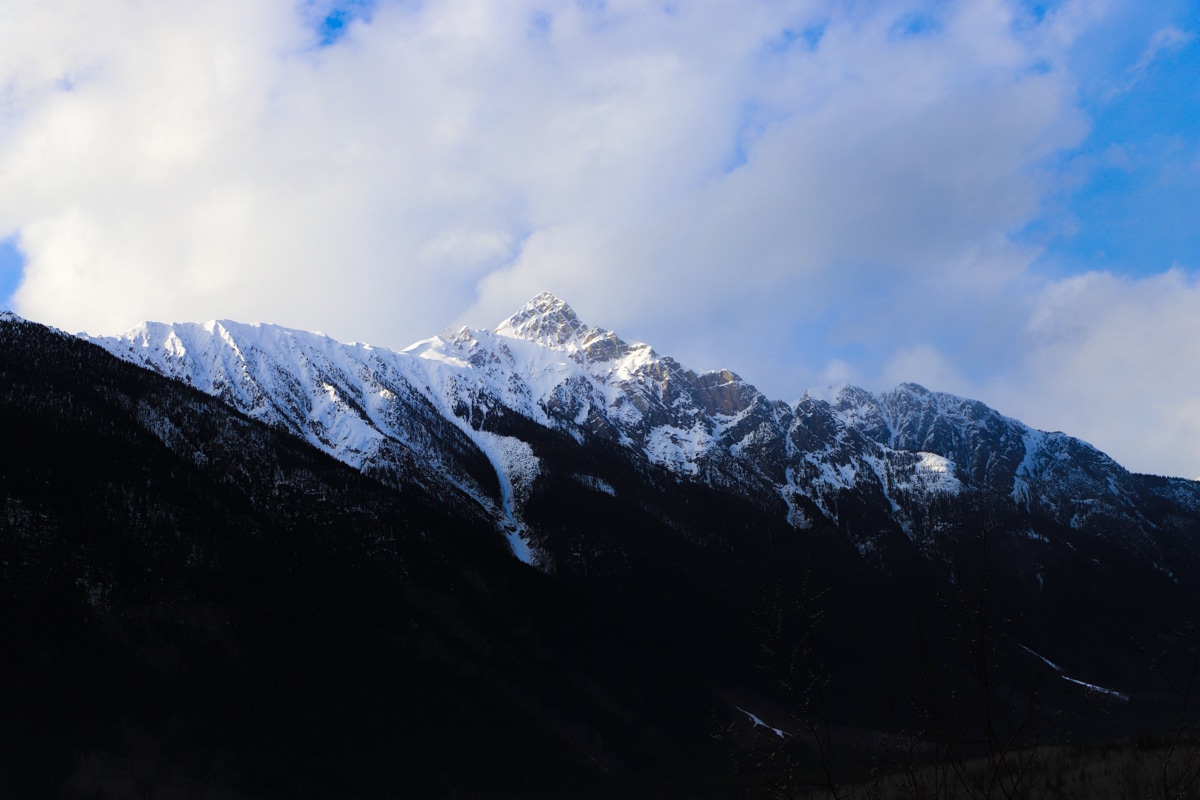 Dark snow covered mountains and blue sky with white clouds.