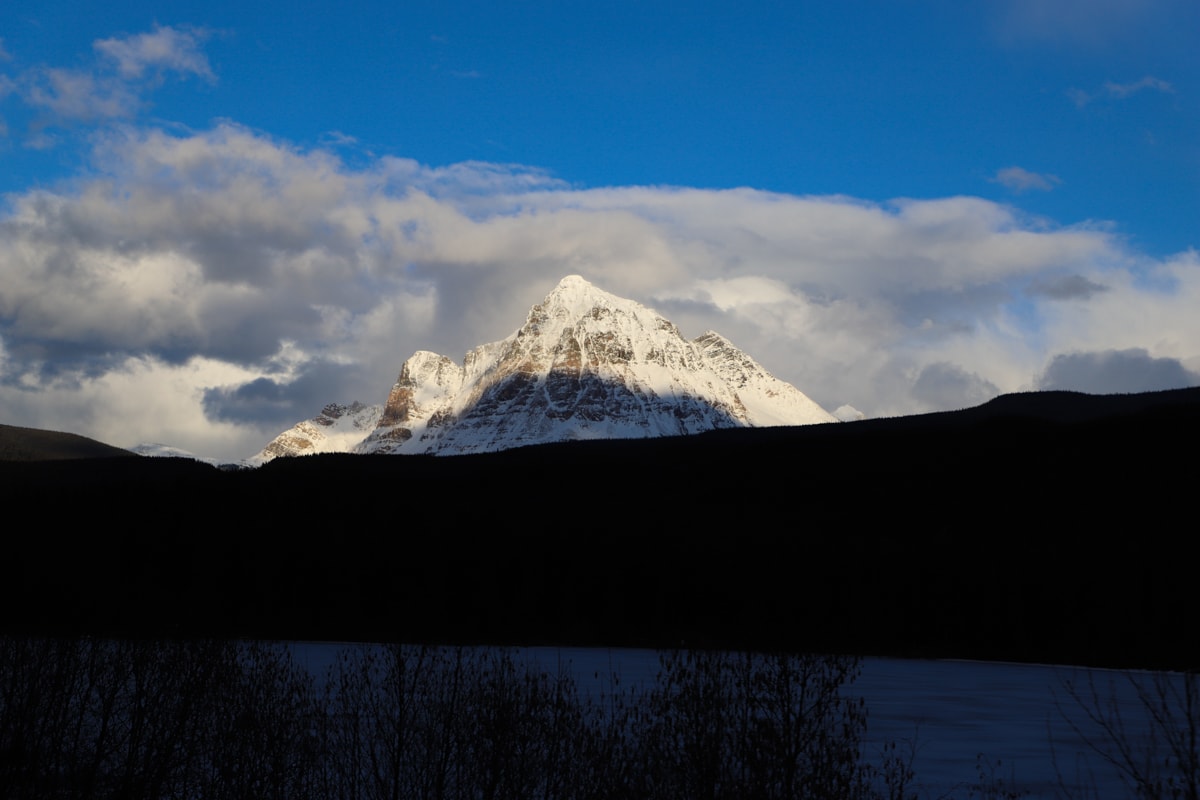 Sun shining on snow covered mountains and blue sky with white clouds.