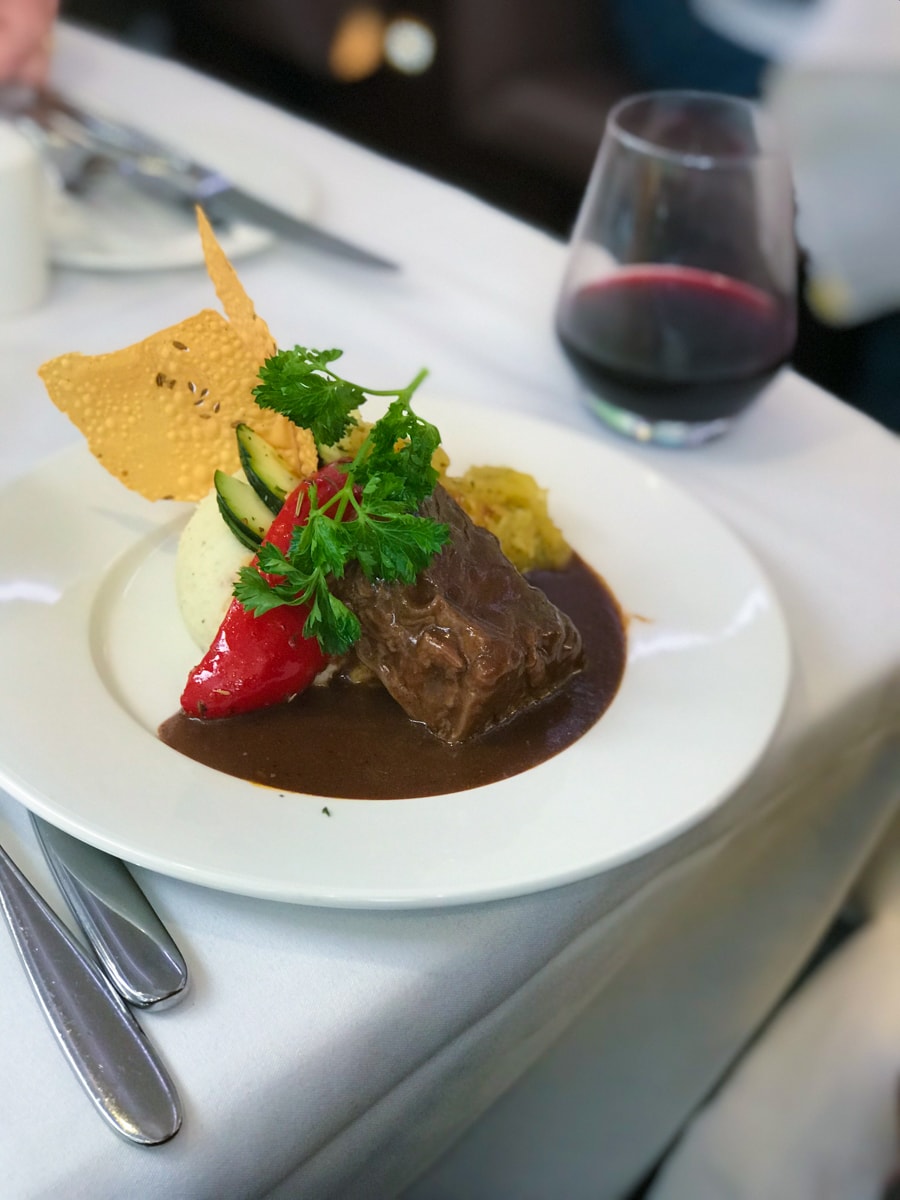 Short ribs and pepper with mashed potatoes and parmesan cheese crisp on white plate with glass of wine.