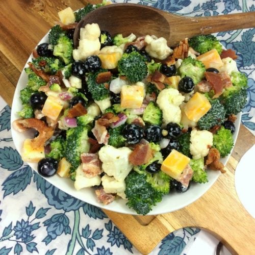 broccoli salad with cheese cubes in a white bowl on a cutting board