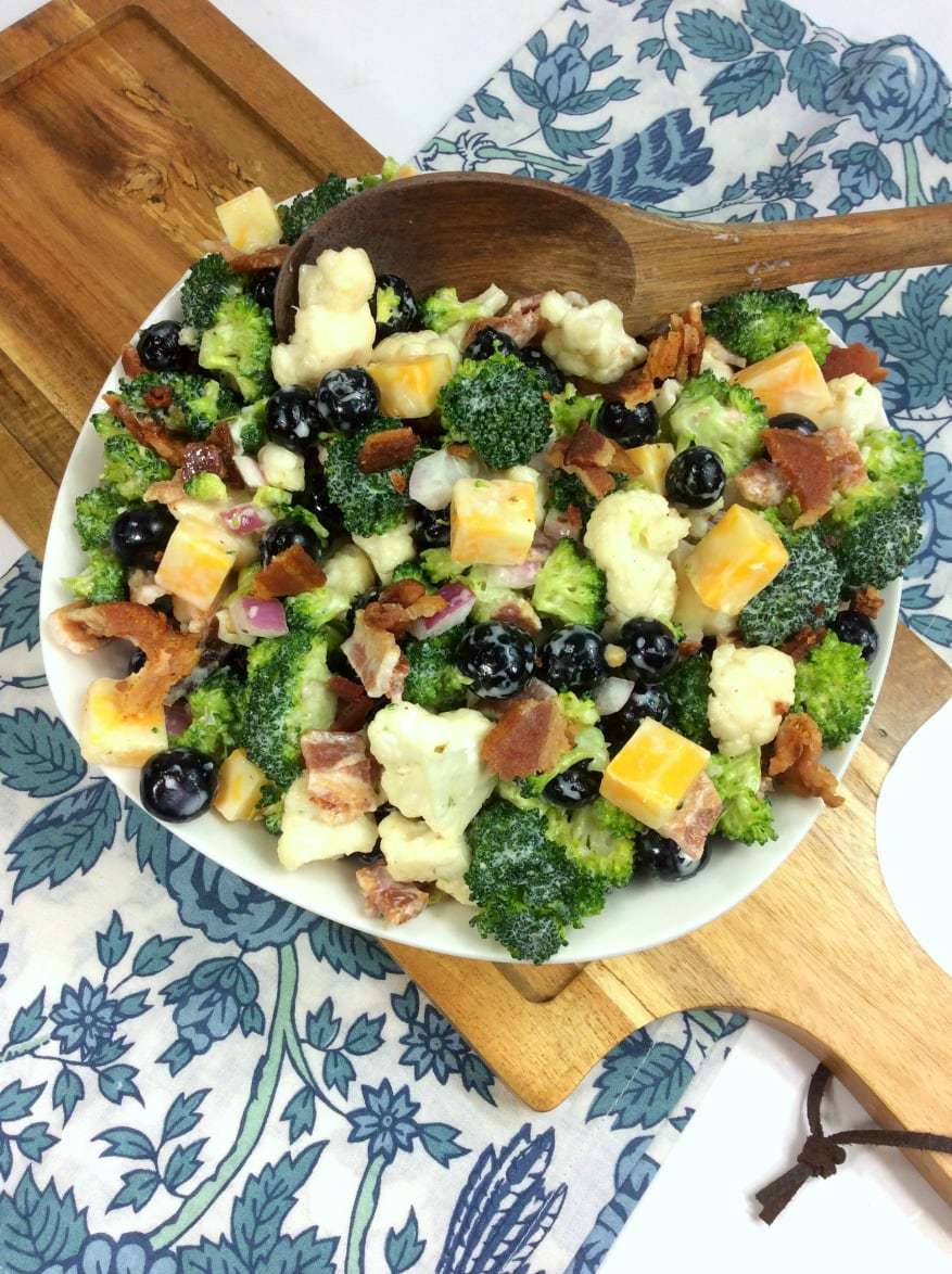 broccoli salad with cheese cubes in a white bowl on a cutting board