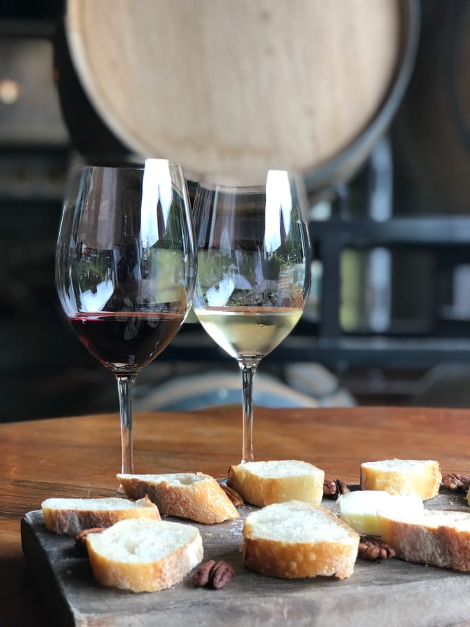 Glass of white wine with a glass of red wine and bread with butter and nuts on wood block.