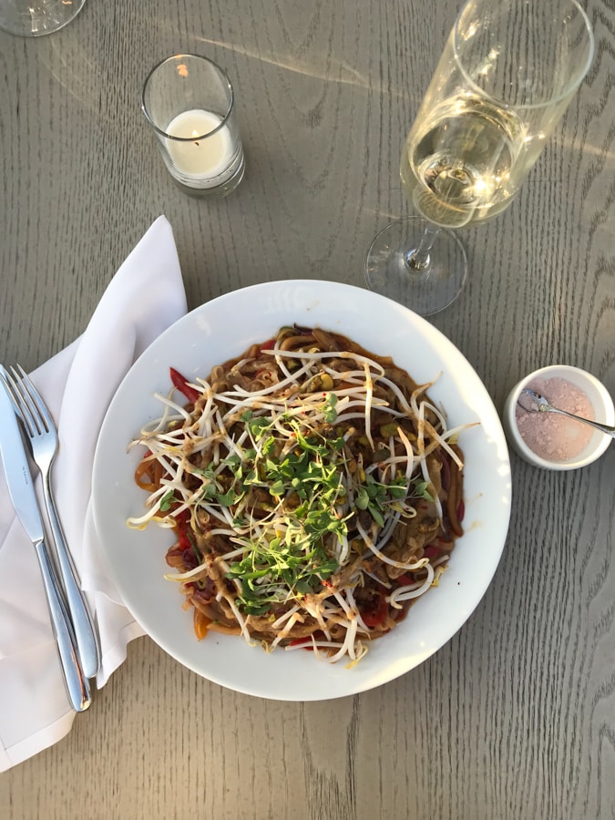 Plate of vegan food on a grey wood table with a glass of white wine and a candle.