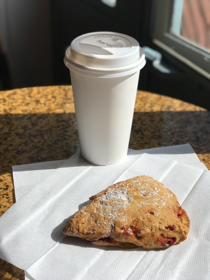 Coffee in a white to-go cup with a scone on a napkin.