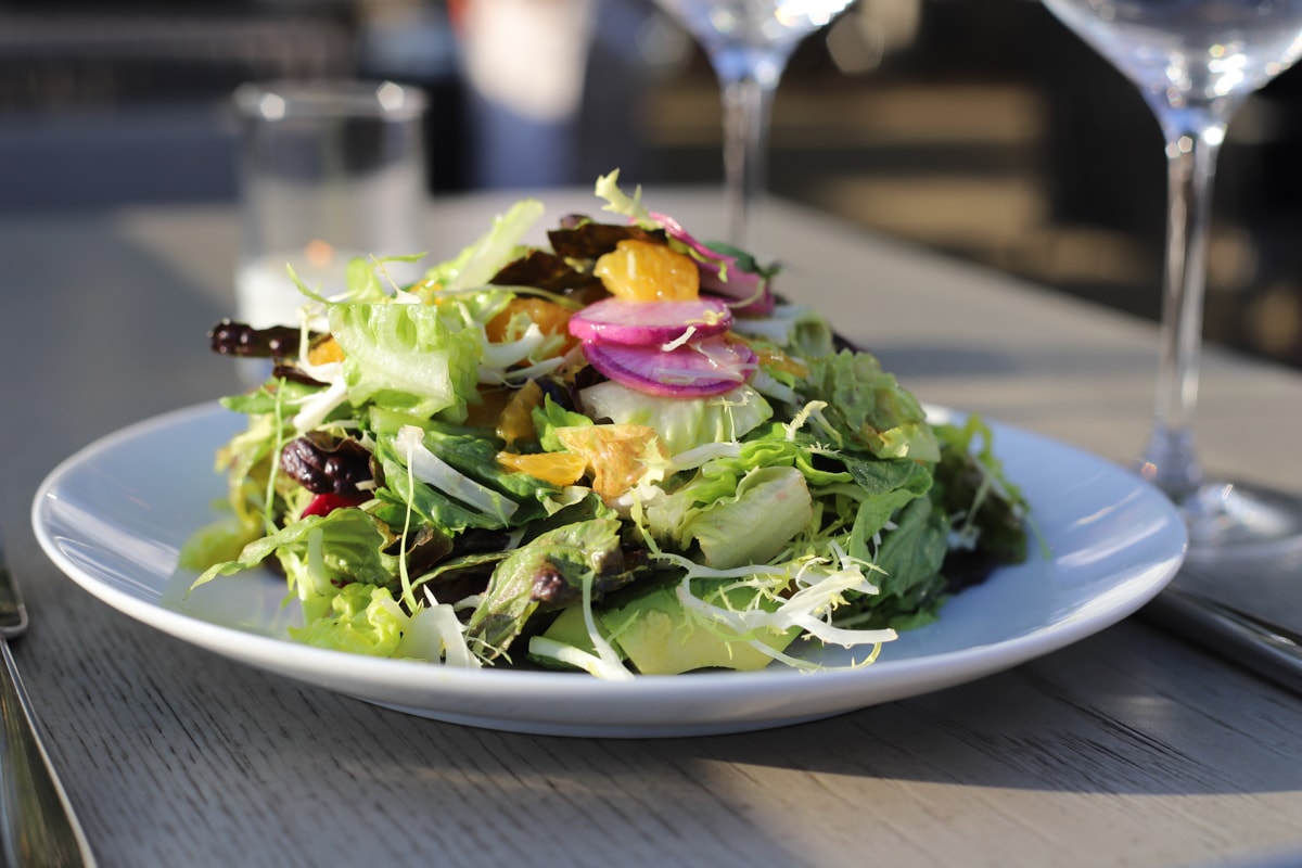 Salad on a white plate on a gray wood table with water glasses.