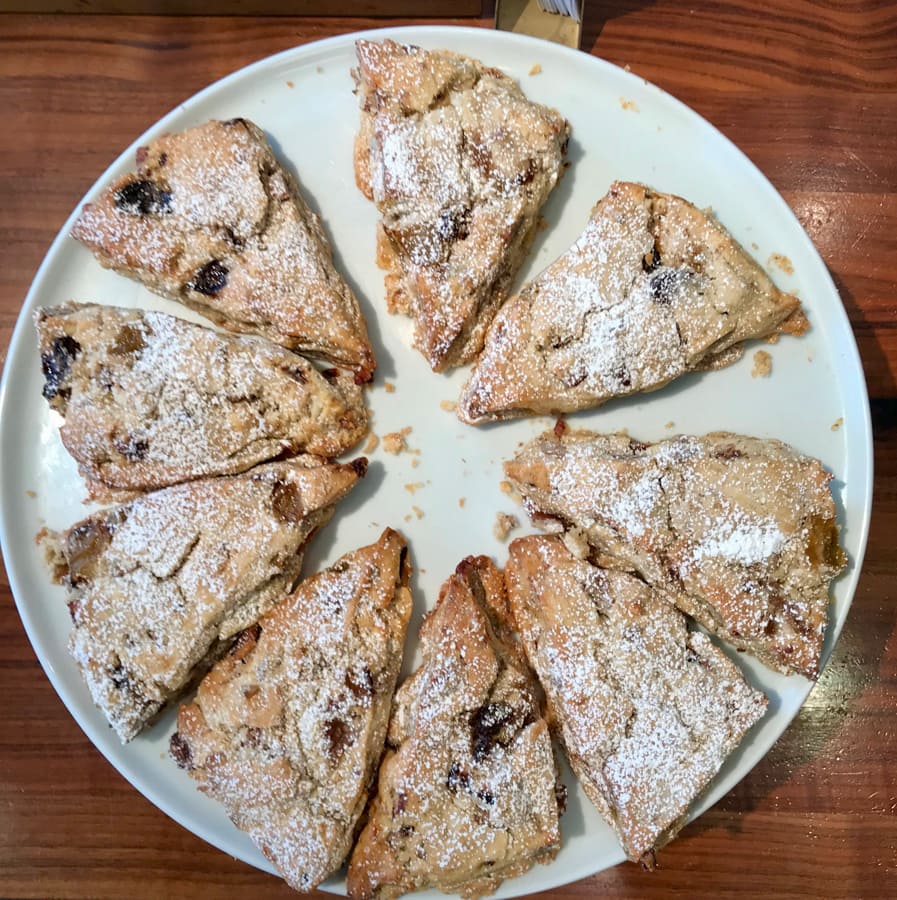 Scones with powdered sugar on a white plate on a wood table.