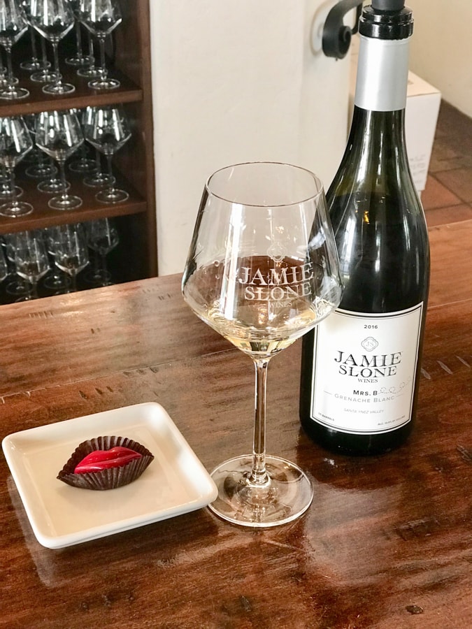 Bottle of wine with white wine in glass and candy on plate on bar.