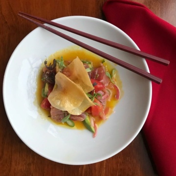 raw tuna and veggies in sauce in white bowl with chopsticks on red material