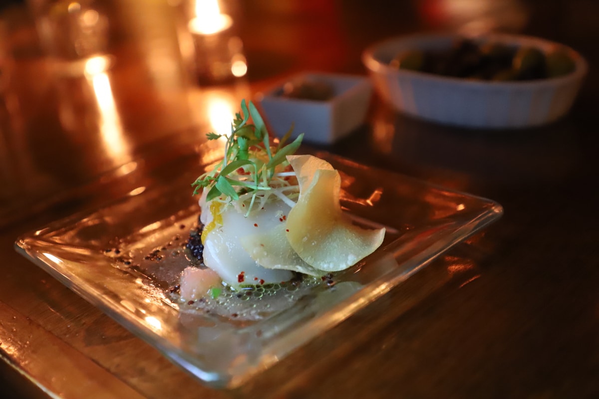 Scallop on plate with potato chip and candle in background.