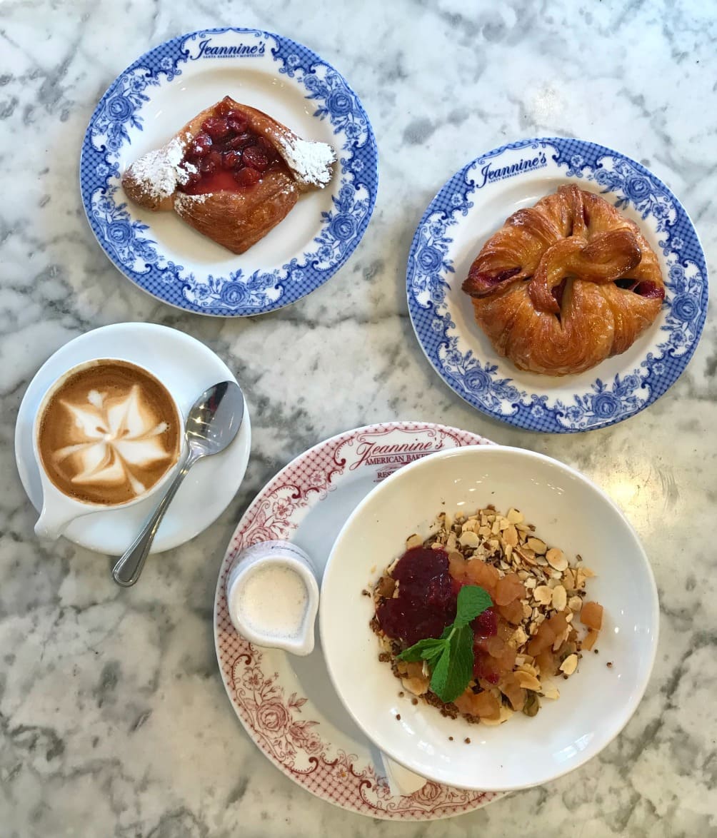 Pastries and granola in bowl with a cappuccino on a marble table.