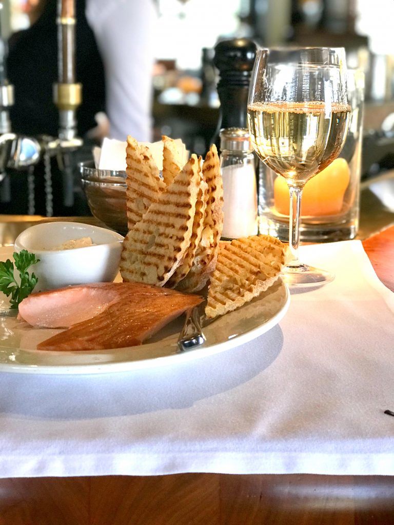 Salmon, bread, and a glass of wine on a white paper placemat.