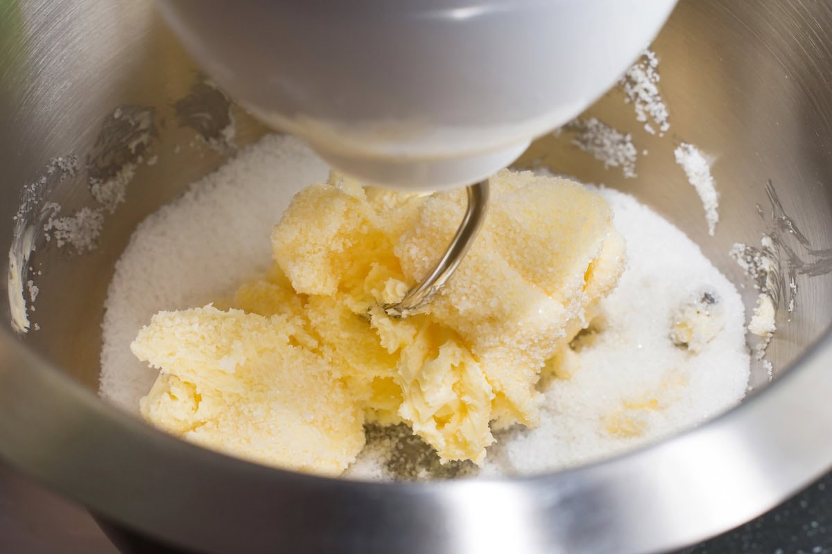 Mixing butter and sugar with a hand beater in a stainless bowl.
